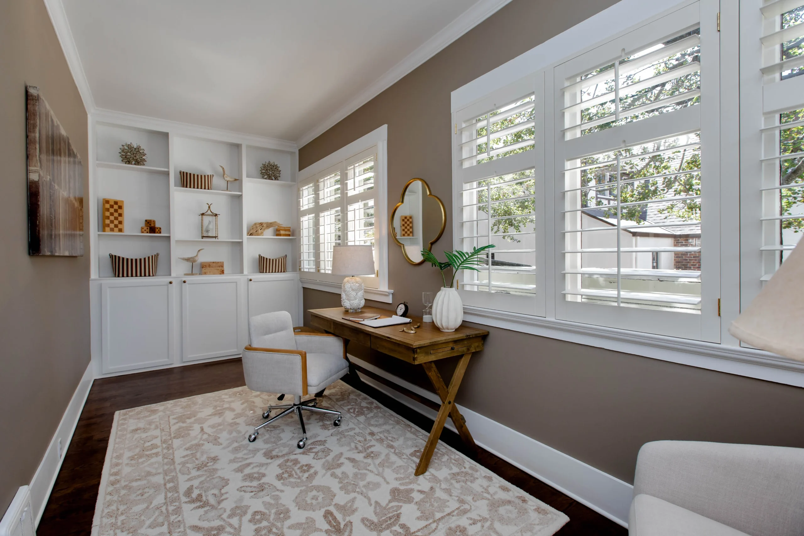 Bright home office with large windows, white shelves, and a wooden desk.
