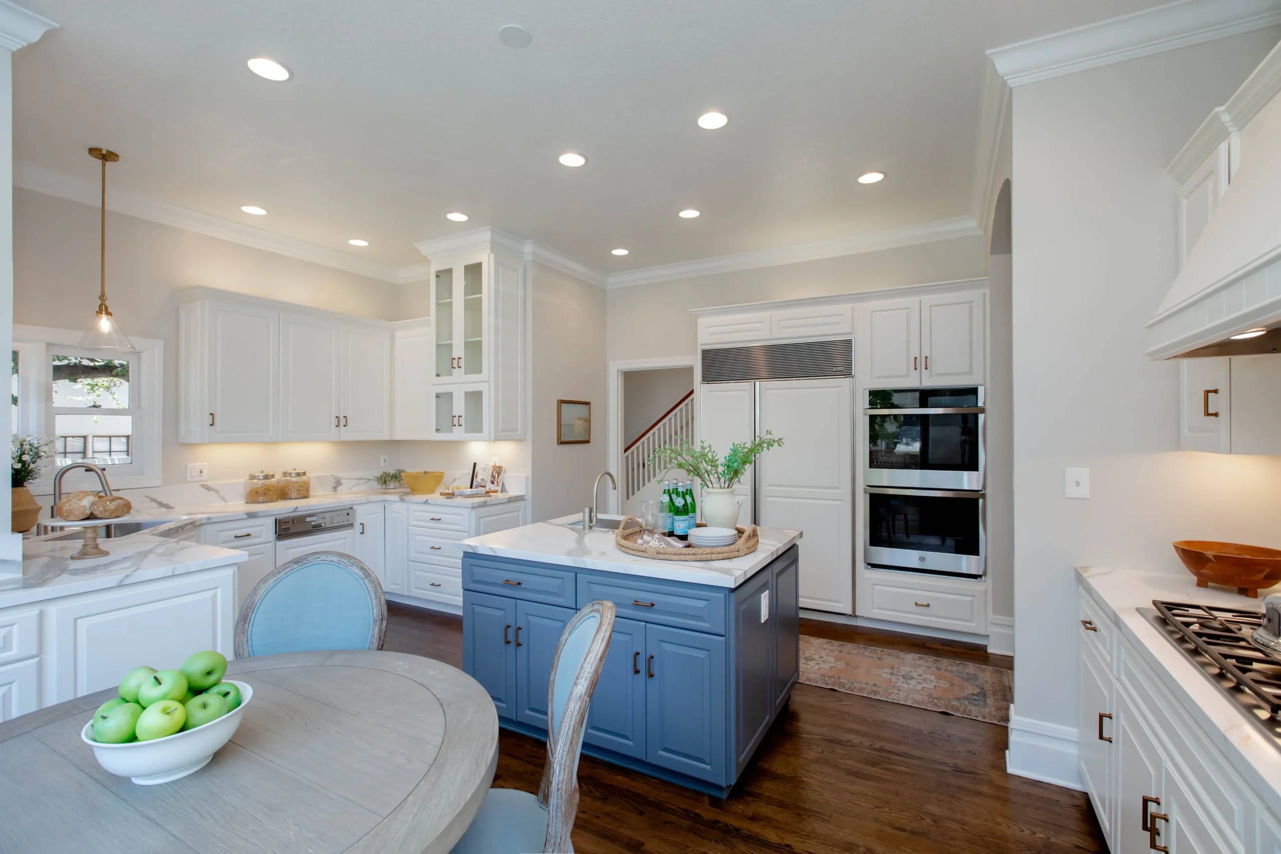 Modern white kitchen with blue island and stainless steel appliances.