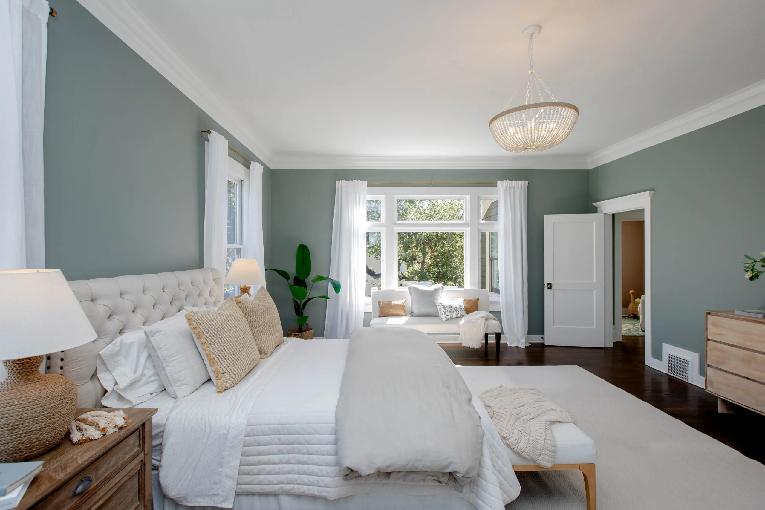 Elegant bedroom with soft green walls, white bedding, and natural light from large windows.