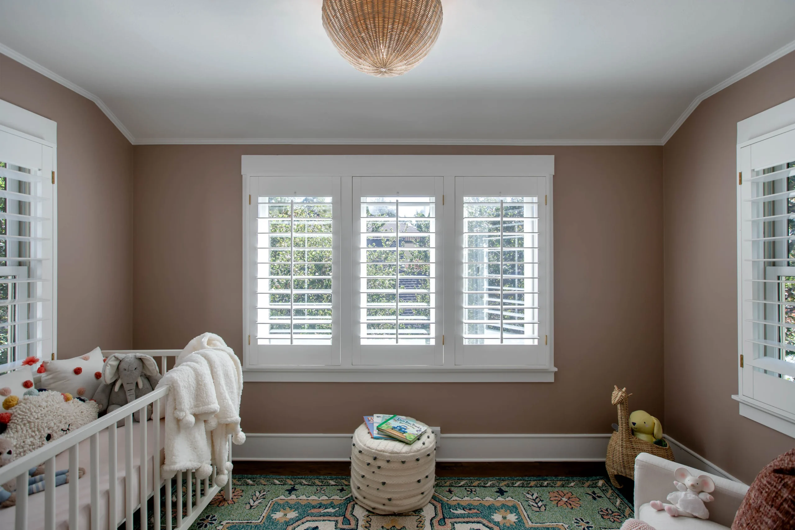 Bright nursery with beige walls, white shutters, and plush toys.