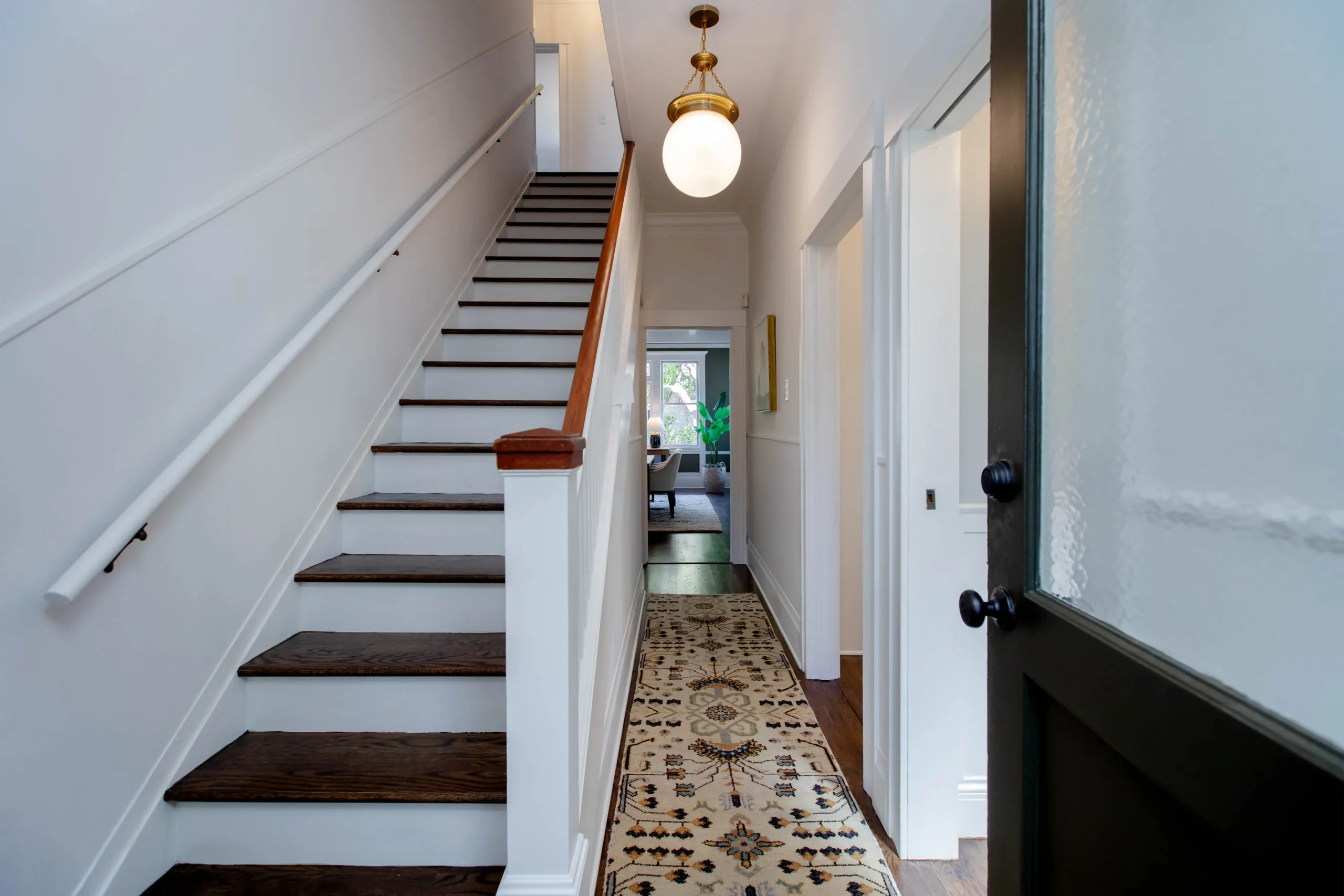 Bright hallway with staircase and hanging light fixture in a modern home.
