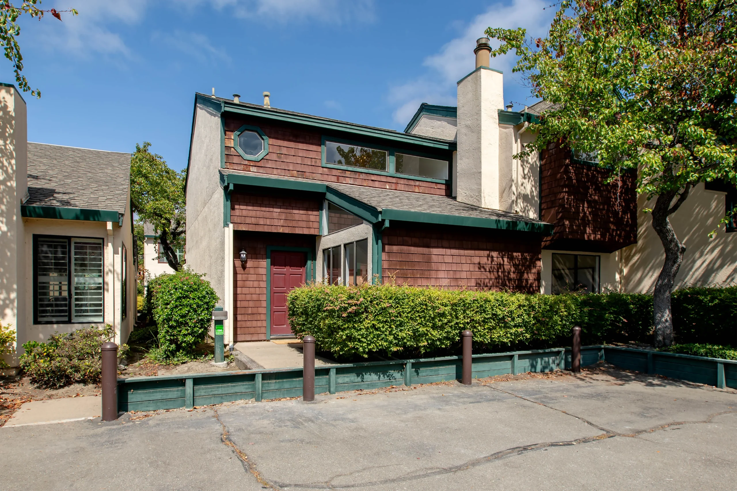 Charming multi-level house with green trim and red siding in a sunny neighborhood.