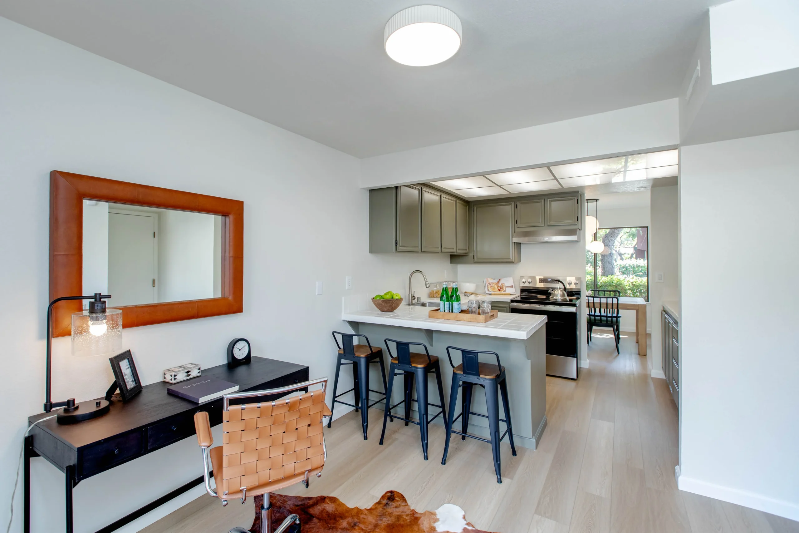 Modern kitchen and workspace with bar stools and a desk in a bright apartment.