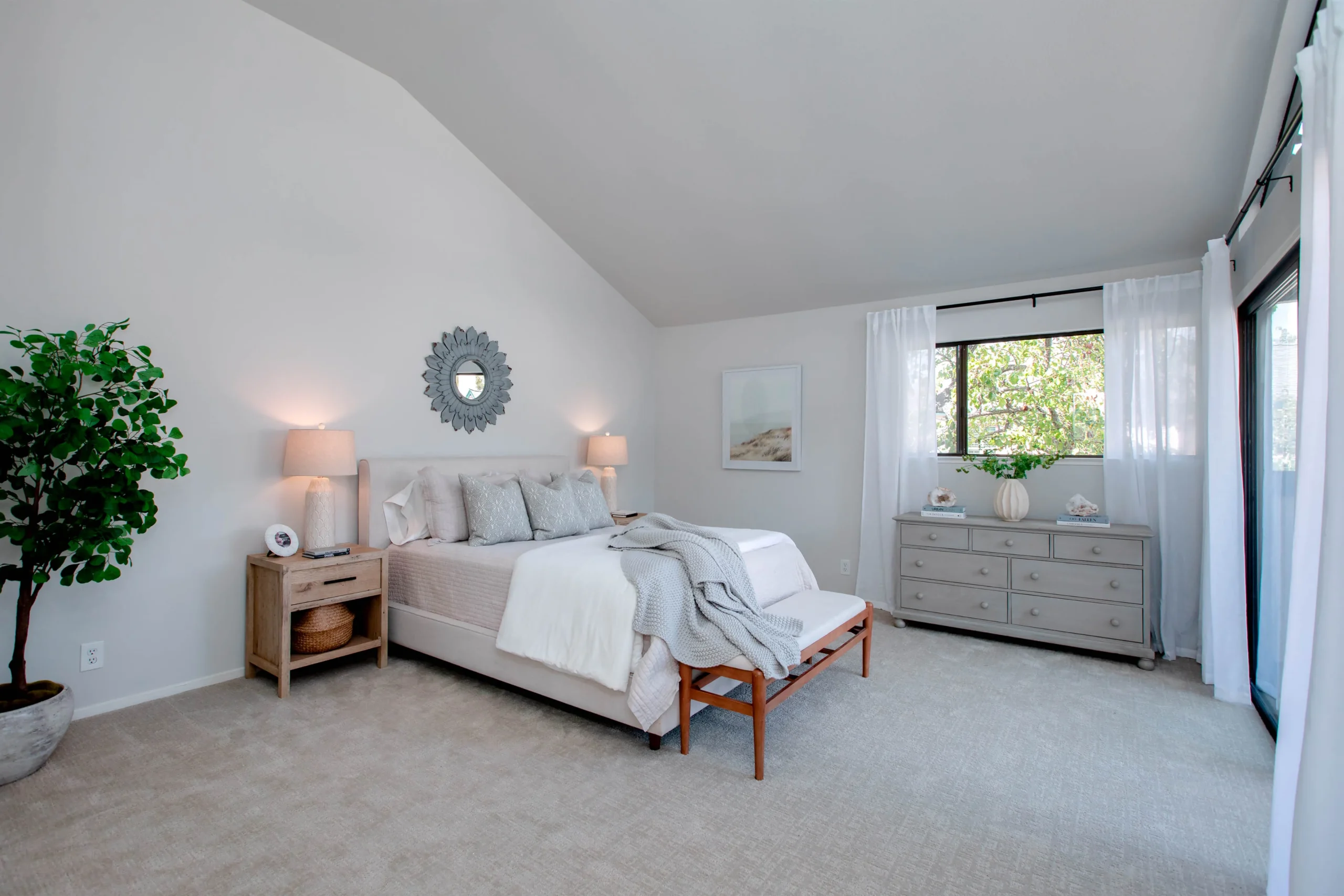 Bright bedroom with white decor and large window, cozy and inviting.