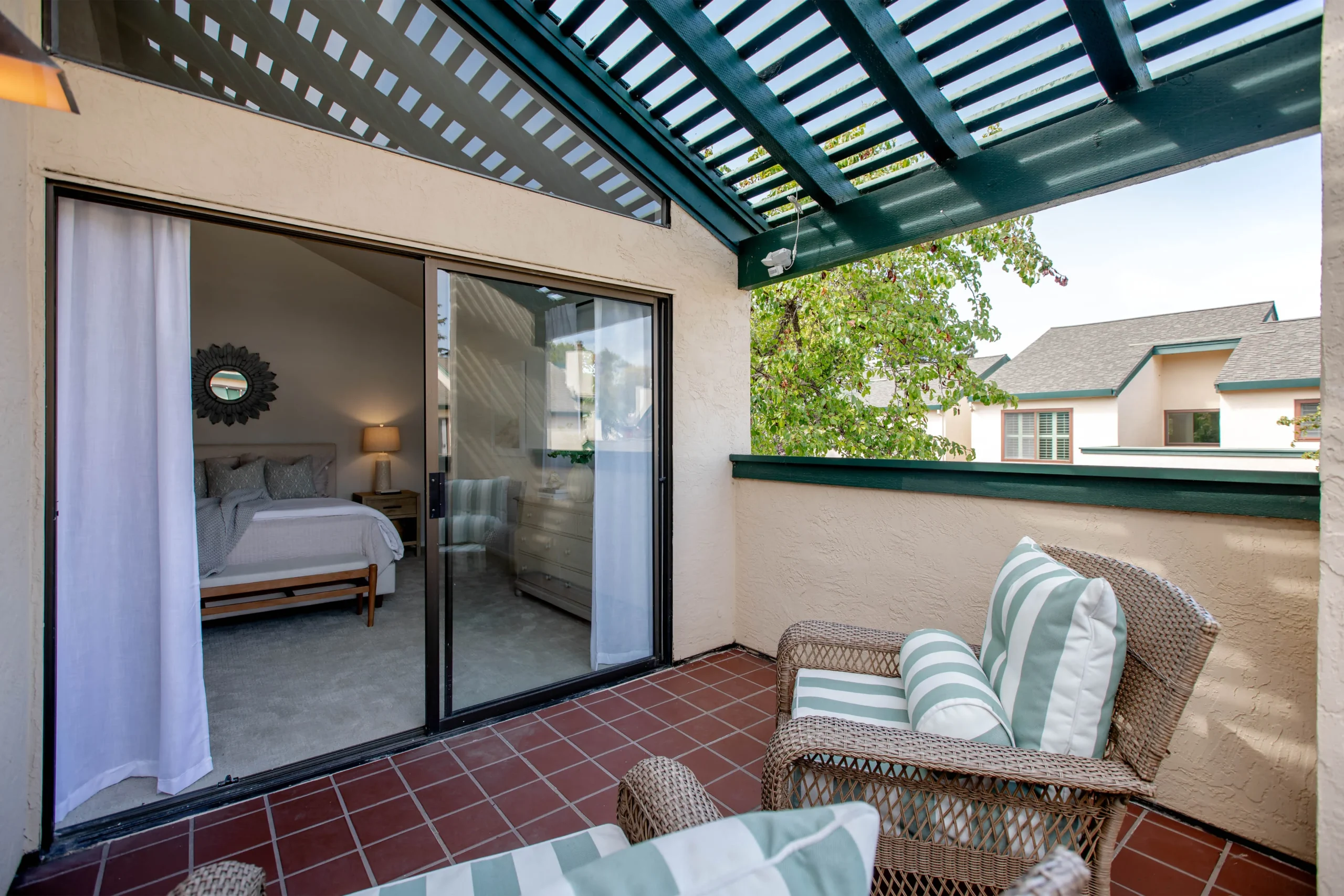 Balcony with wicker chairs and striped cushions overlooking a residential neighborhood.