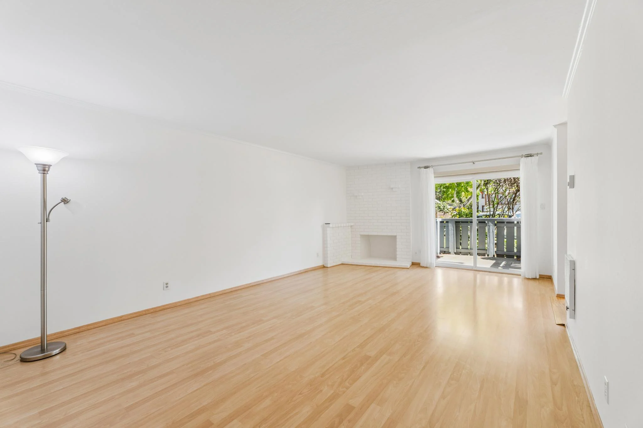 Spacious empty living room with white walls and wooden floor.