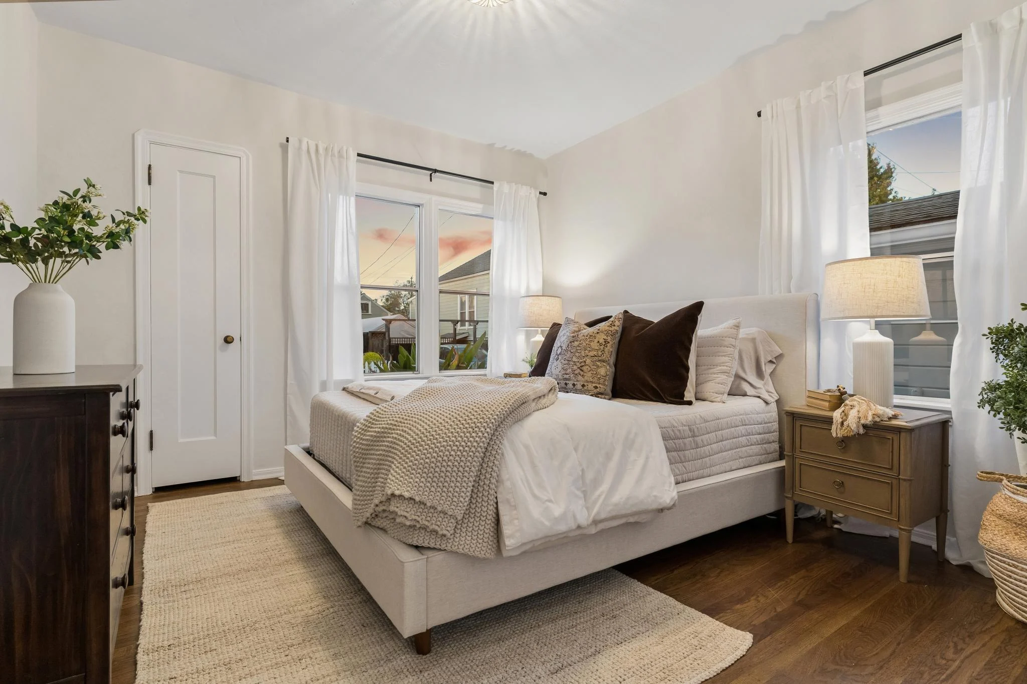 Bright bedroom with white walls, large windows, and cozy bedding.