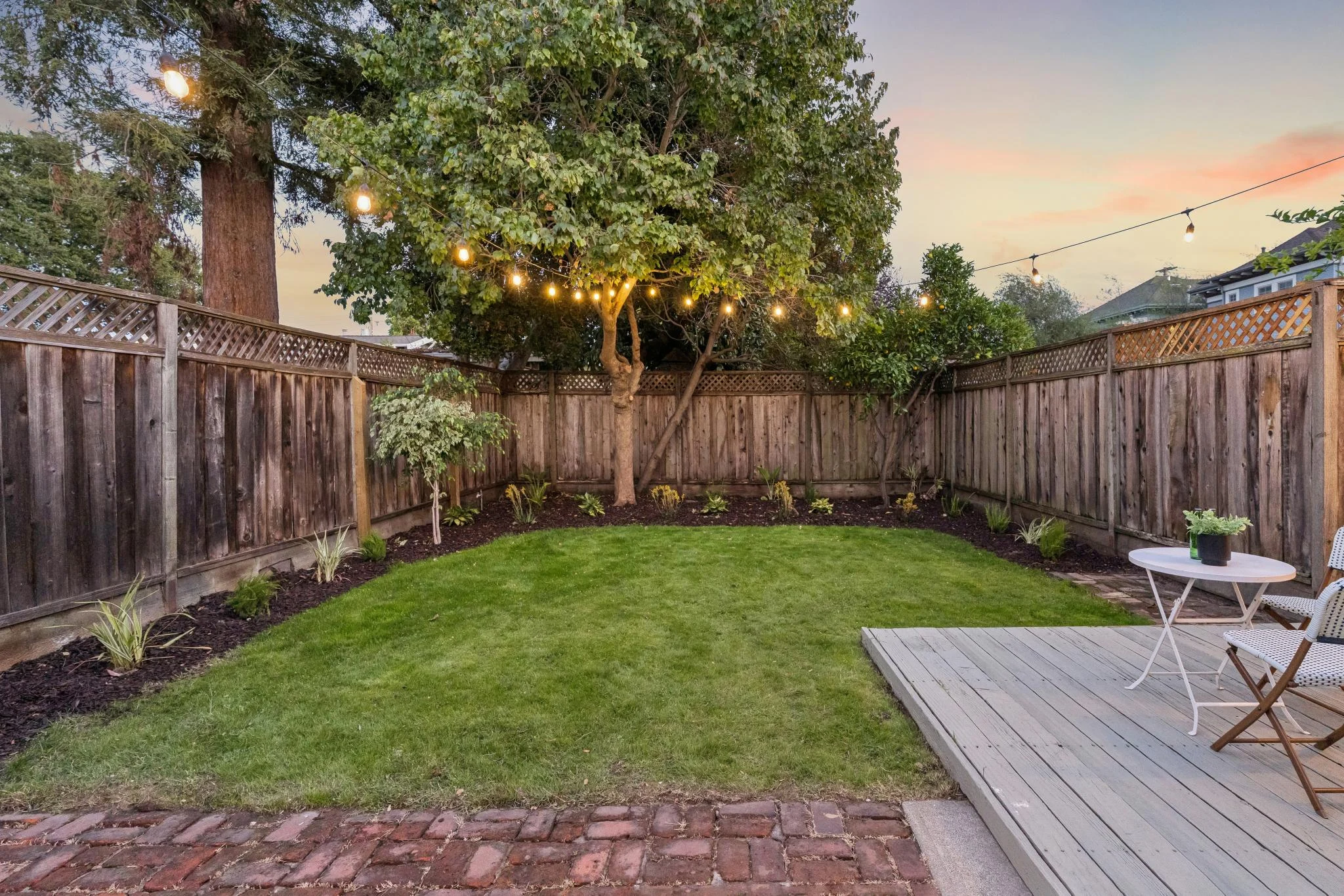Beautiful backyard with lush green lawn, string lights, and cozy seating area at sunset.