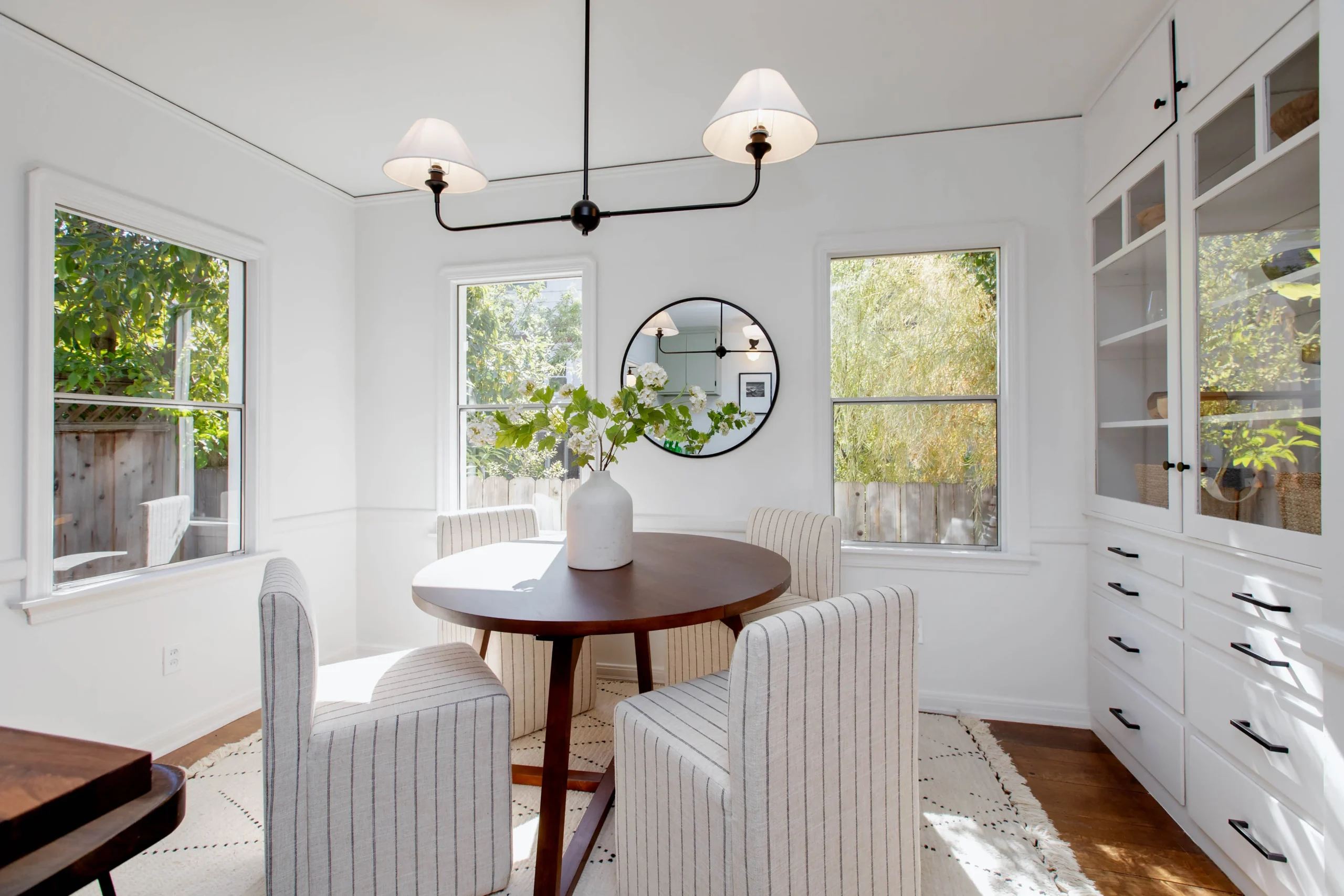 Bright dining room with white walls, round wooden table, and four striped chairs.