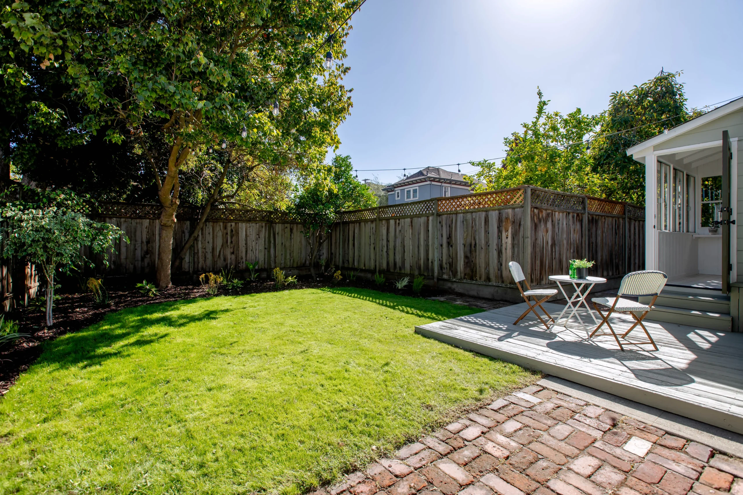 Beautiful backyard with lush green lawn, patio furniture, and mature trees under sunny sky.